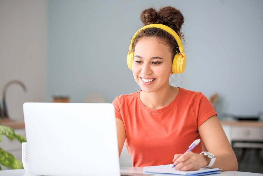 A student exploring her Online M.Ed. Degree Programs Options on a laptop with yellow headphones